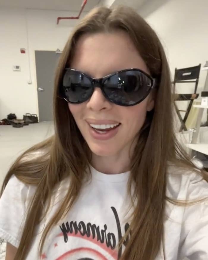 Julia talks to the camera while wearing sunglasses and a white tee