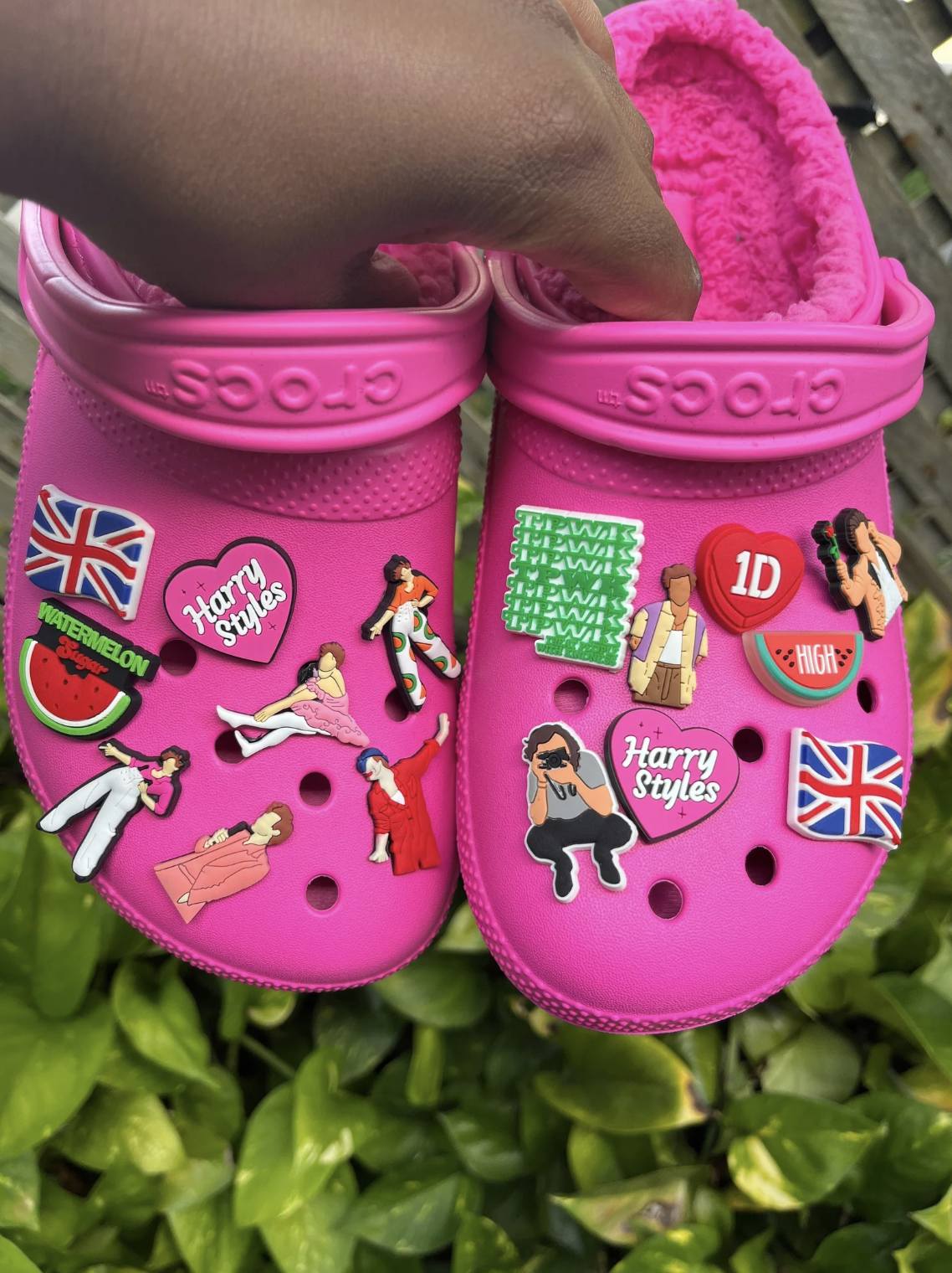 A person holding a pair of Crocs with Harry Styles charms on them