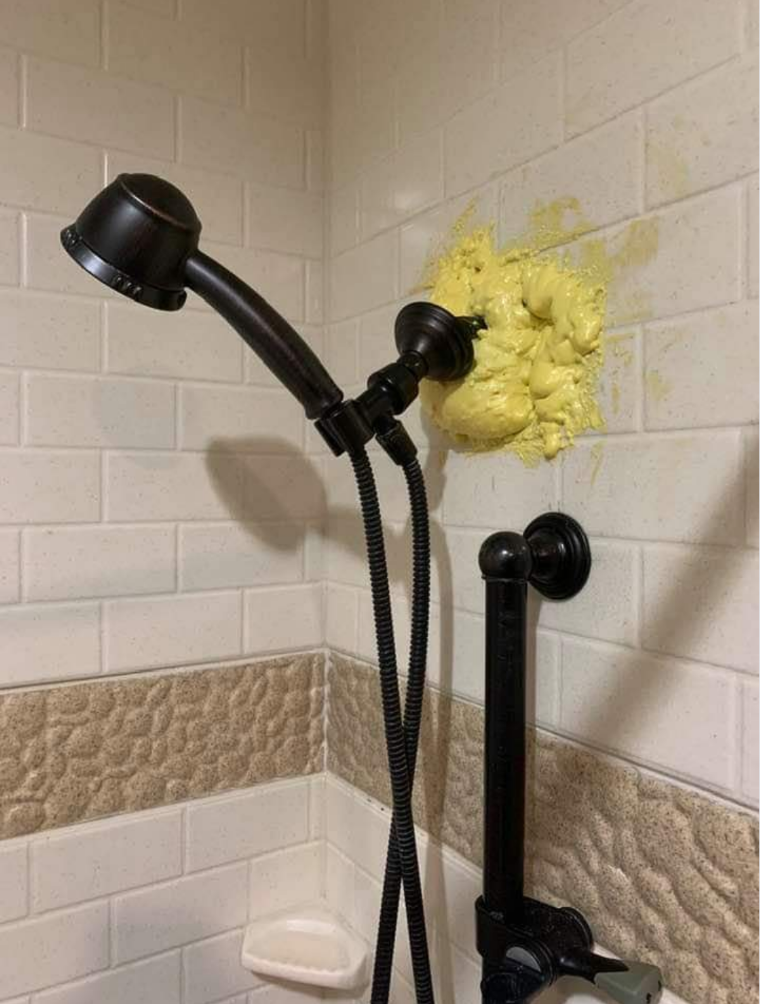 Showerhead with a mound of yellow gunk/foam behind it where it emerges from the wall