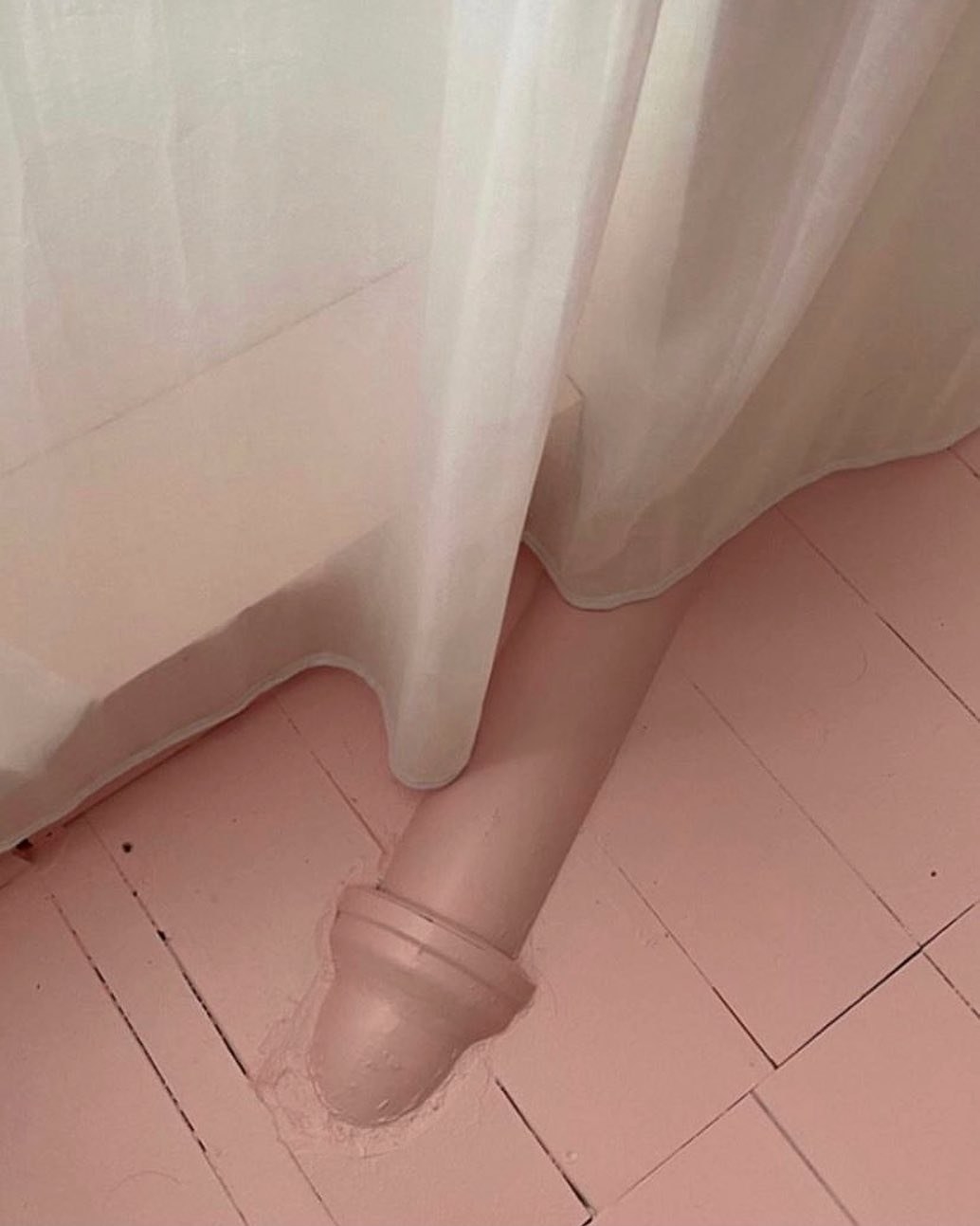 Pipe emerging from a floorboard painted the same color as the floor and looking like a large penis