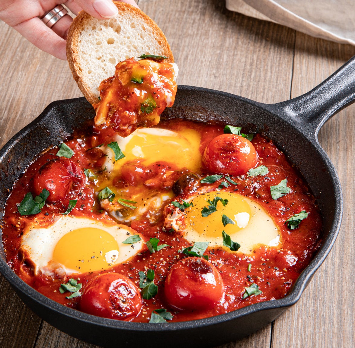 cast iron with three eggs in pool of tomato sauce and small tomatoes