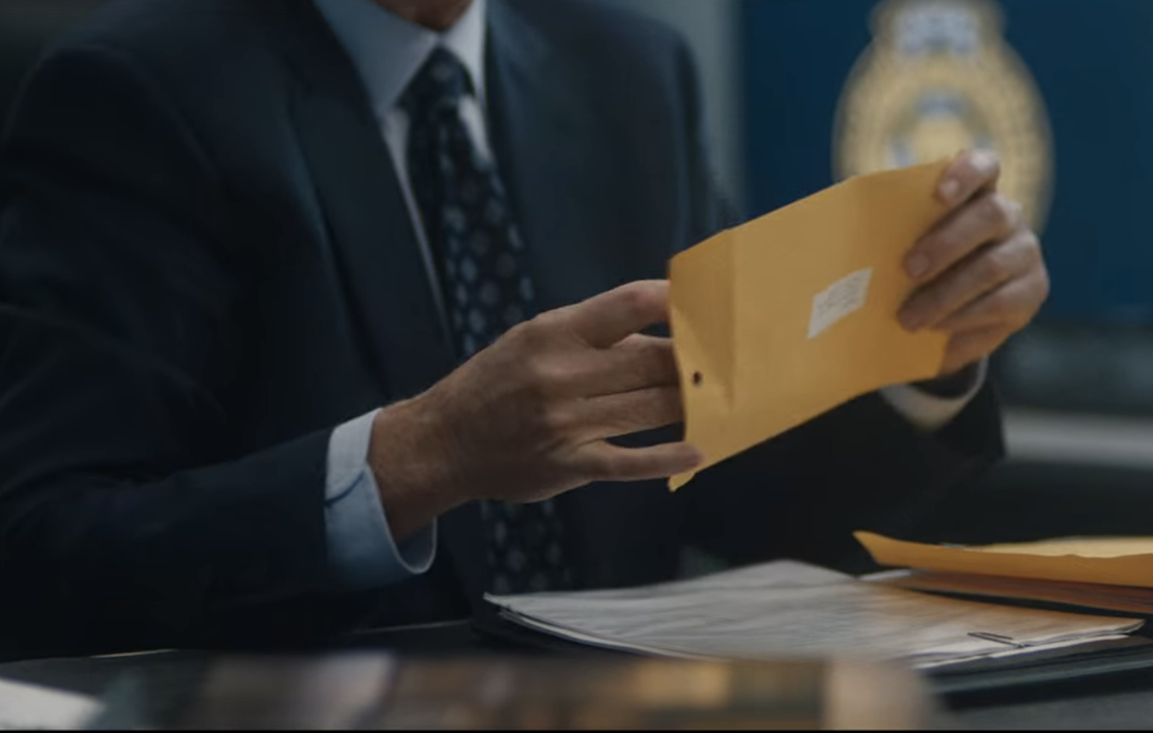 A person in a suit holding an envelope and with the DNA report on a table in front of them