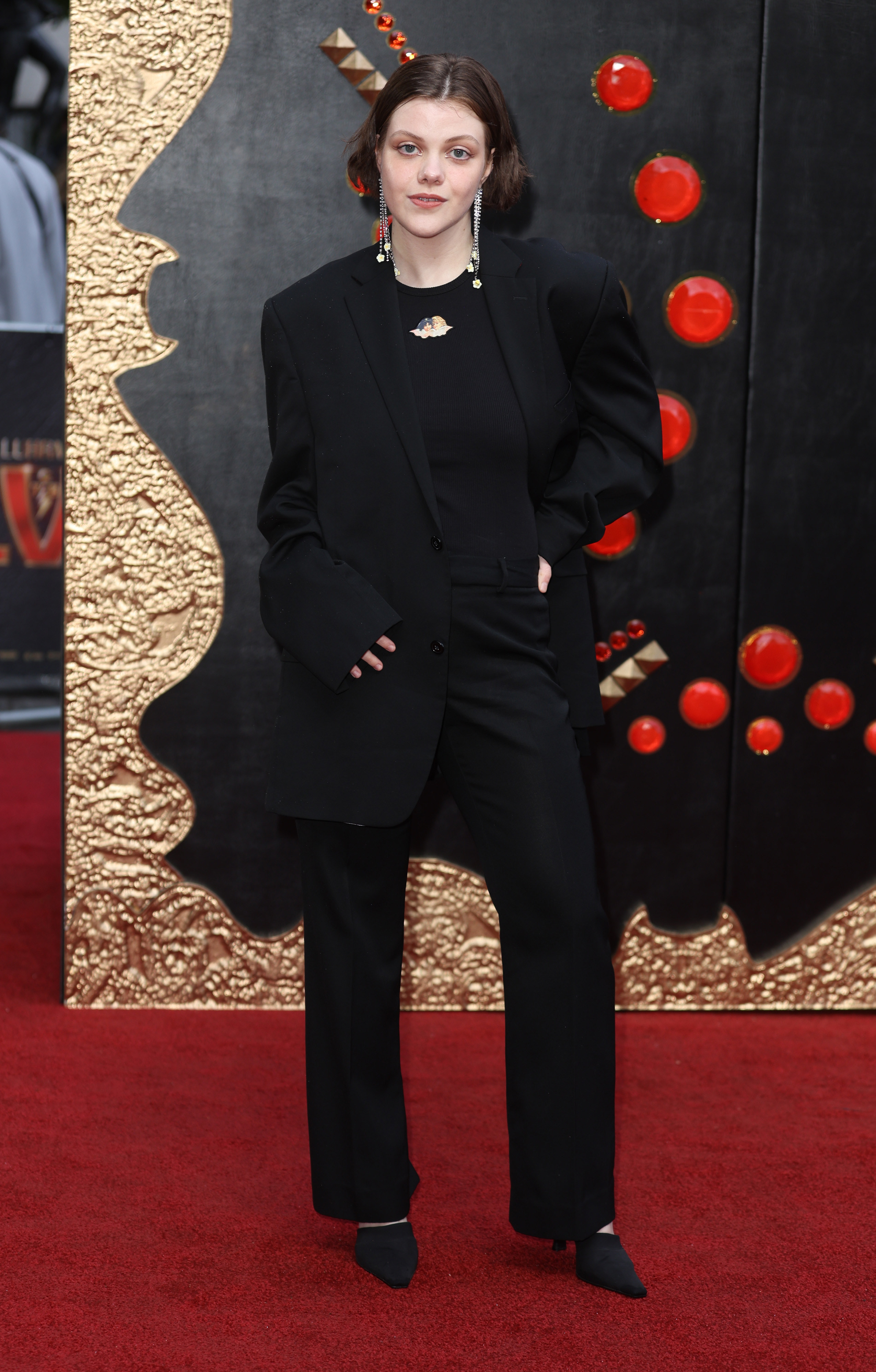 Georgie on the red carpet in black pants, top, and jacket and long earrings