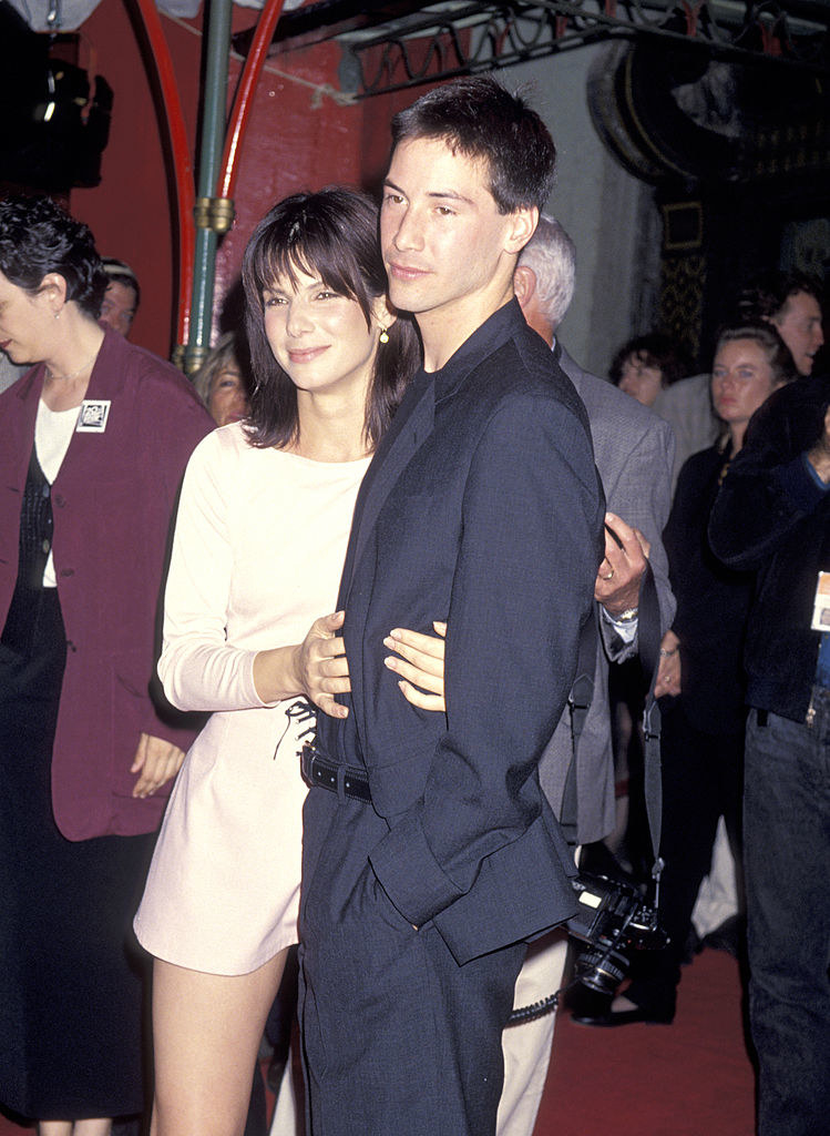 Keanu Reeves and Sandra Bullock with their arms around each other on the red carpet