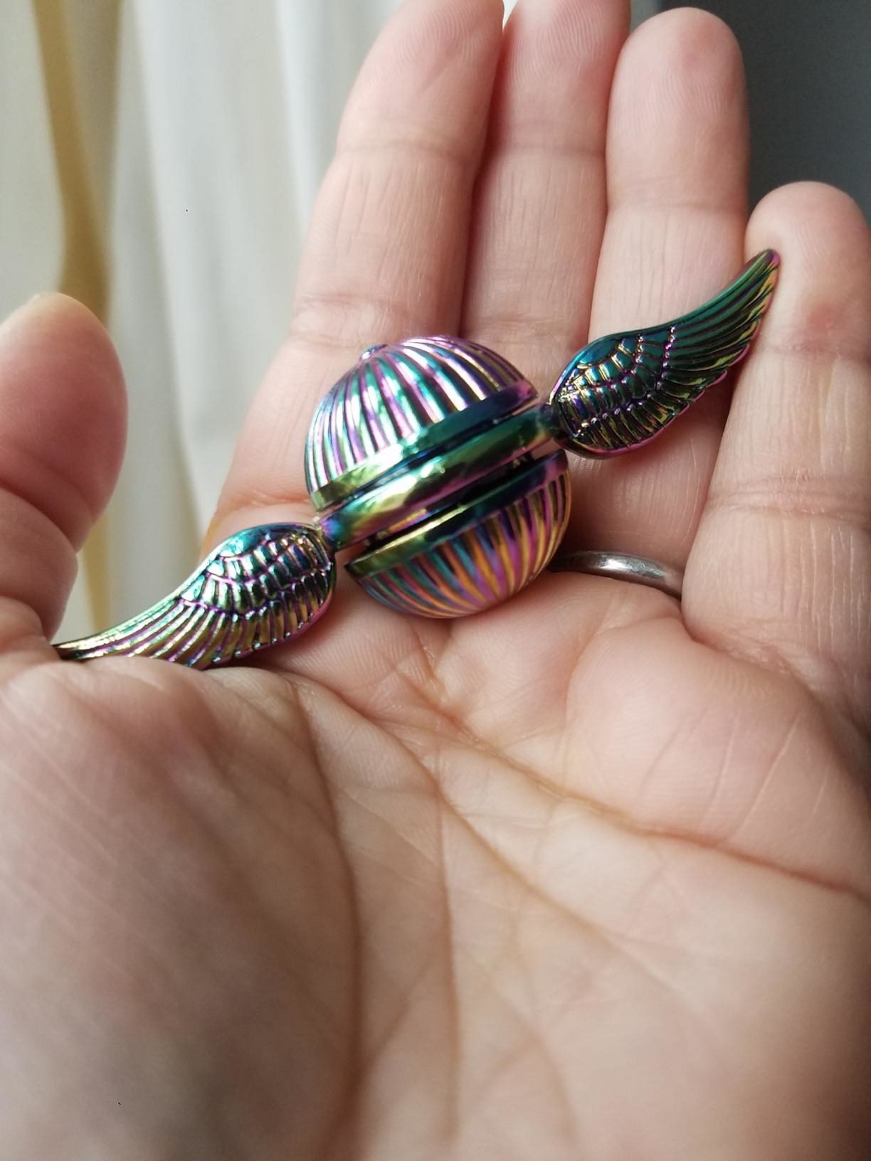 Reviewer holding the rainbow toy that looks like a Flying Snitch with wings coming out of the sides
