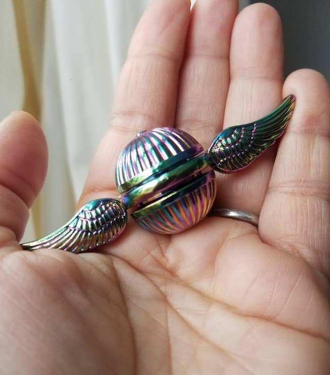 Reviewer holding the rainbow toy that looks like a Flying Snitch with wings coming out of the sides