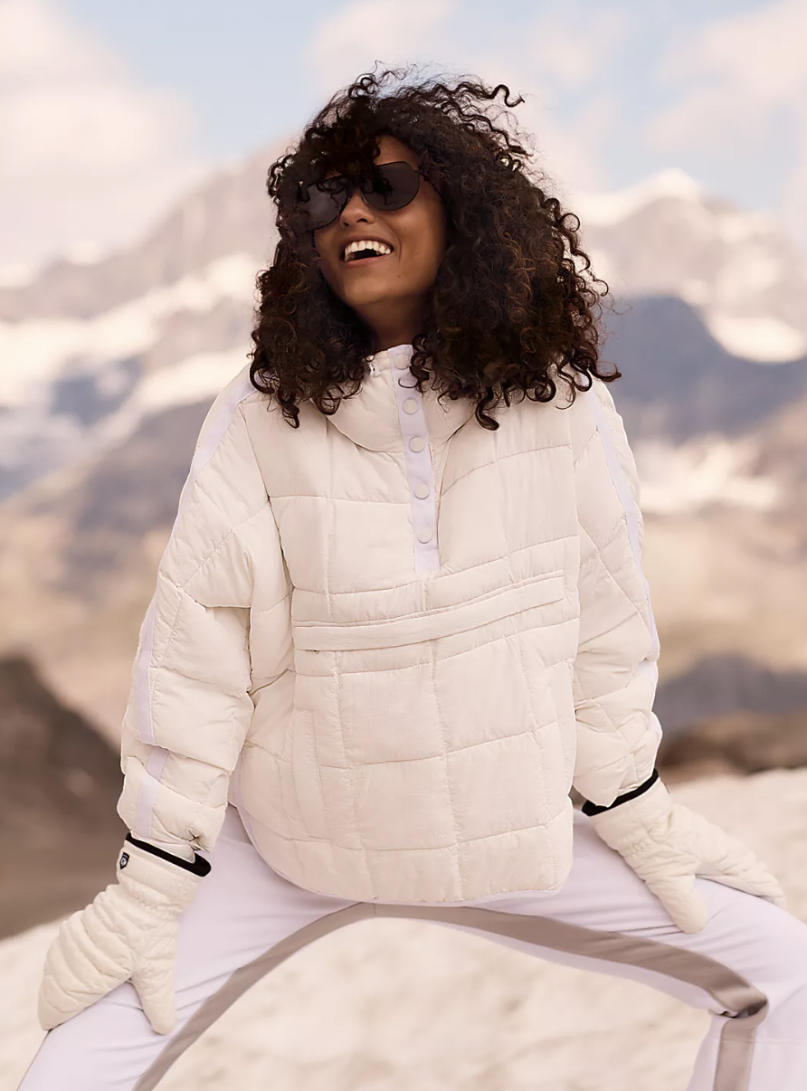 a smiling person frolicking in the snow while wearing the pullover puffer coat