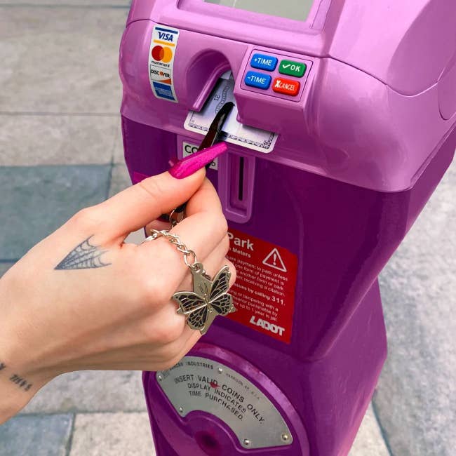 person using a pair of tweezers on a keychain to pull a credit card in and out of a parking meter