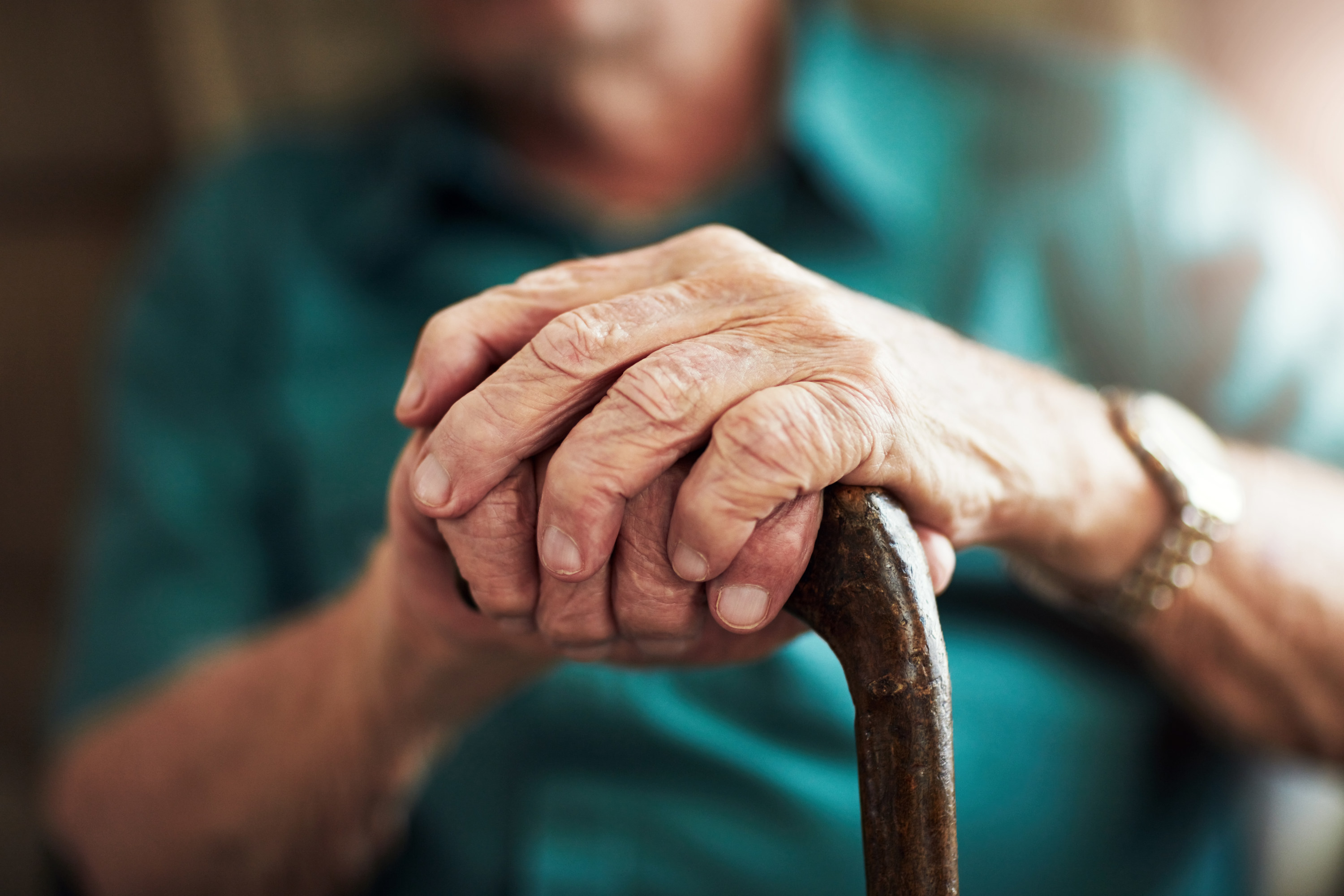 Closeup of an old man&#x27;s hands resting on his cane