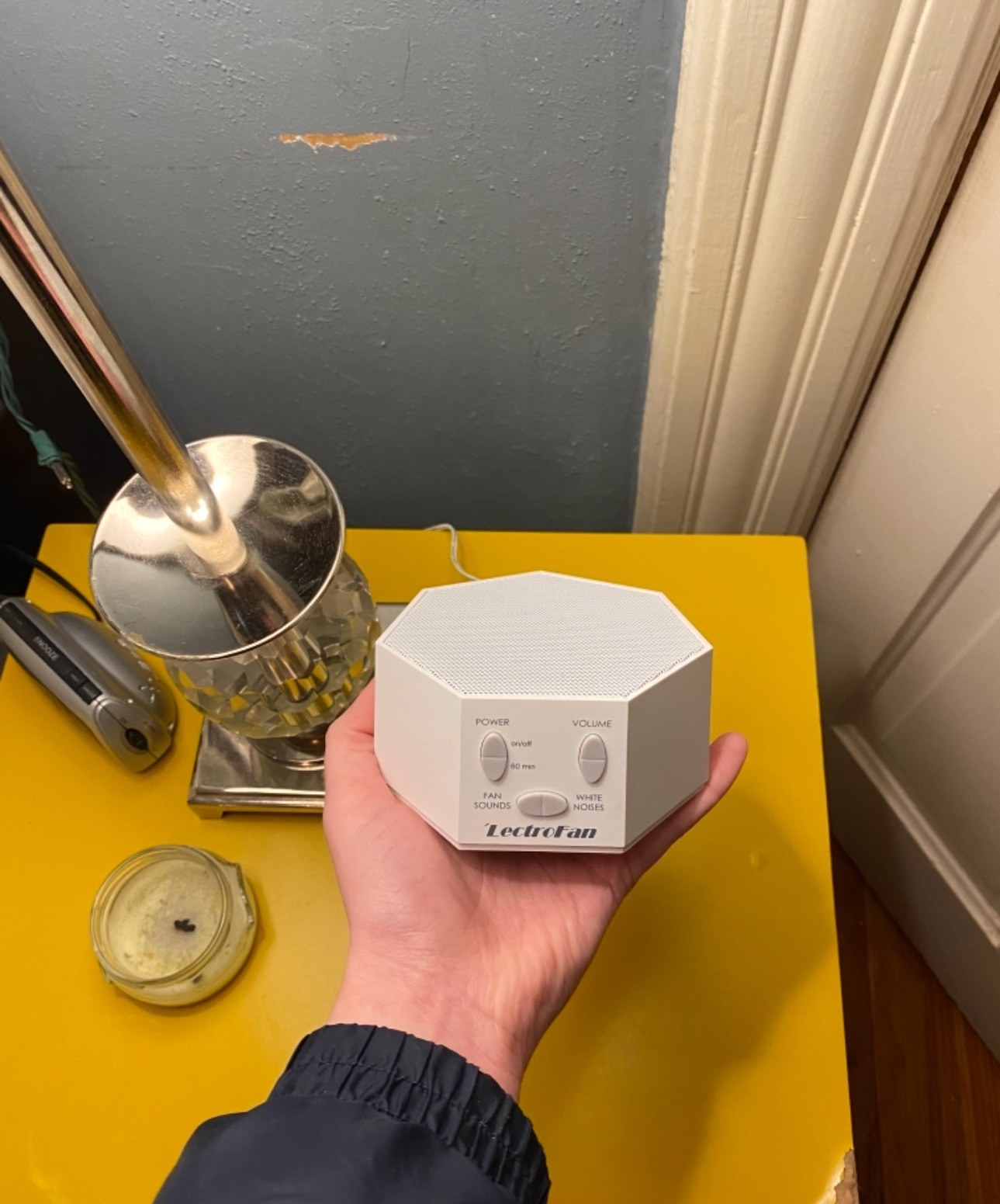 The white noise machine sitting on a side table while Model reads a book