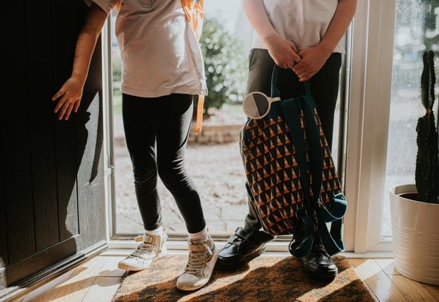 Two young elementary aged children enter through a front door at the same time, after finishing school for the day. They are holding backpacks and wearing school uniforms