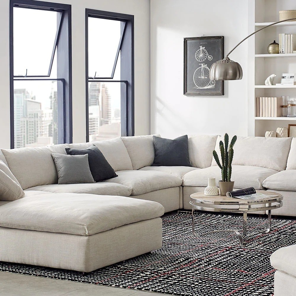 a living room with a u-shaped white couch with blue throw pillows on it and a patterned area rug