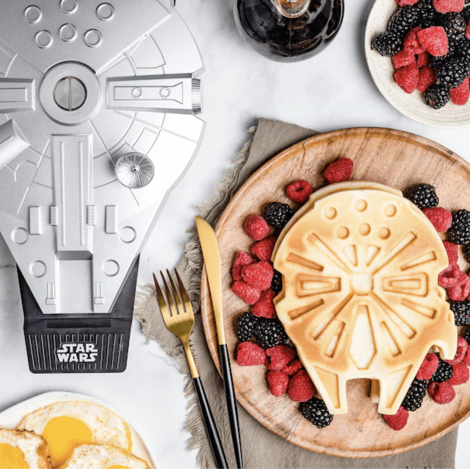 The waffle maker next to a finished waffle surrounded by berries