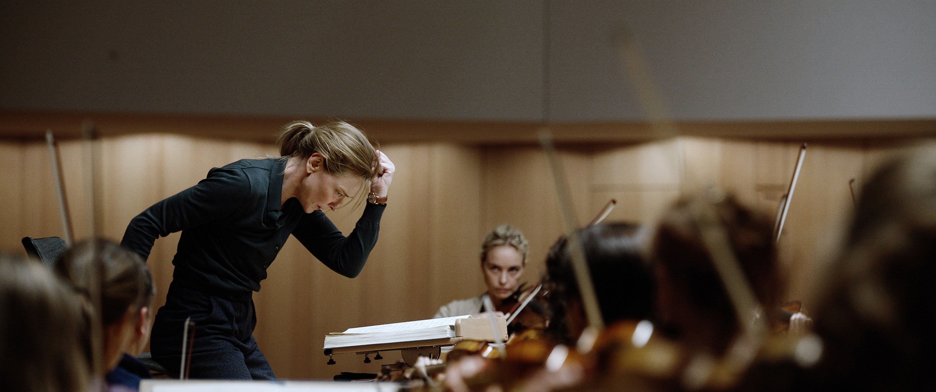 Lydia conducting with her orchestra, Sharon watching from the first violin seat