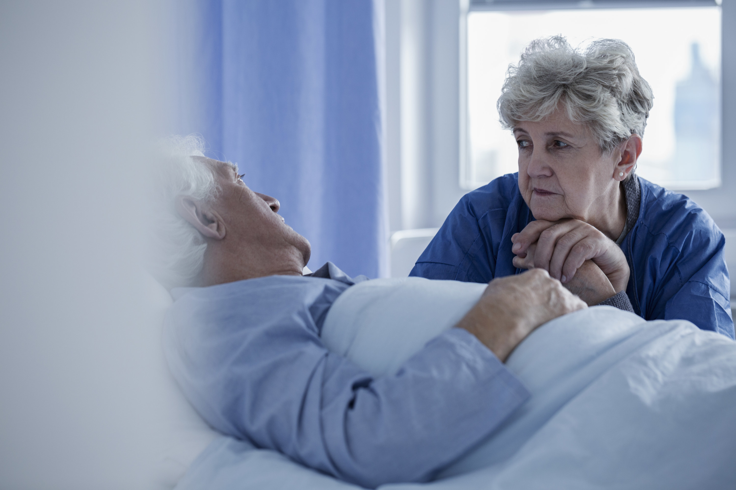 elderly woman with a sick elderly man in a hospital bed