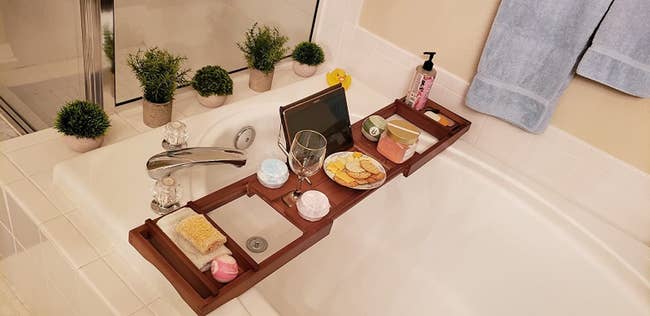 Reviewer image of a wooden bath caddy holding an iPad, washcoth, plant, candle, wine glass, bath salts
