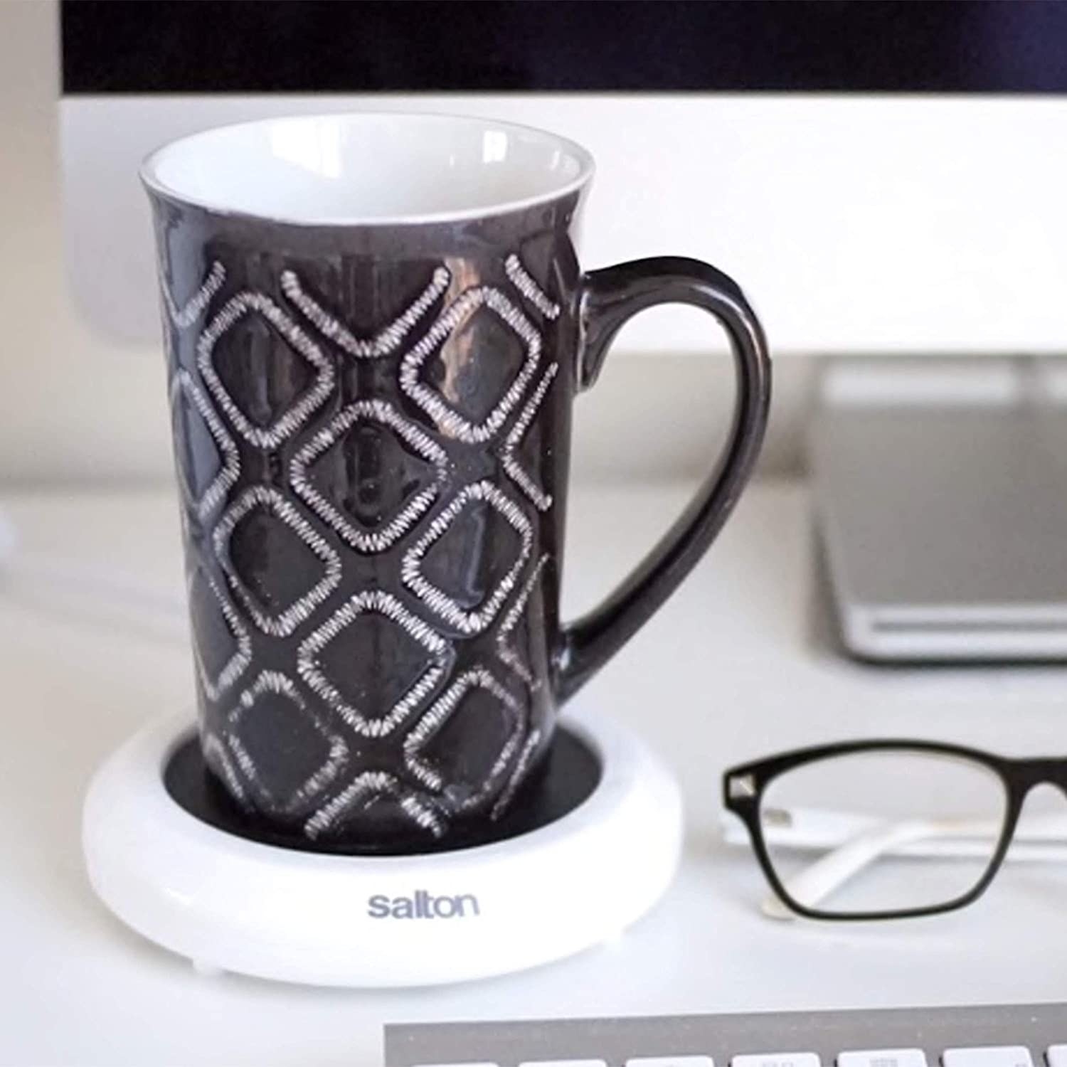a mug on the warmer next to a computer and glasses