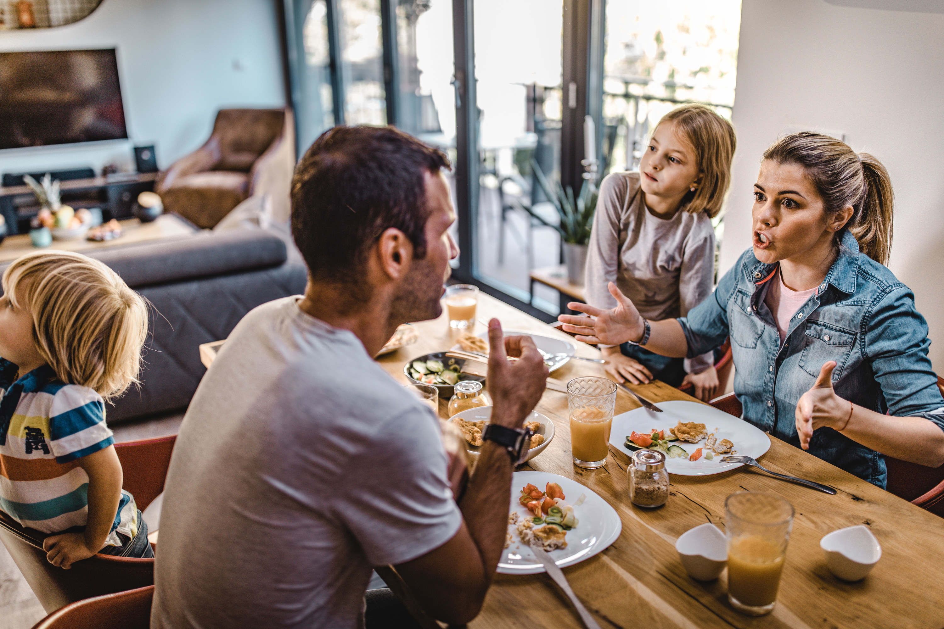 Young couple arguing during lunch time with their children in dining room. Focus is on woman