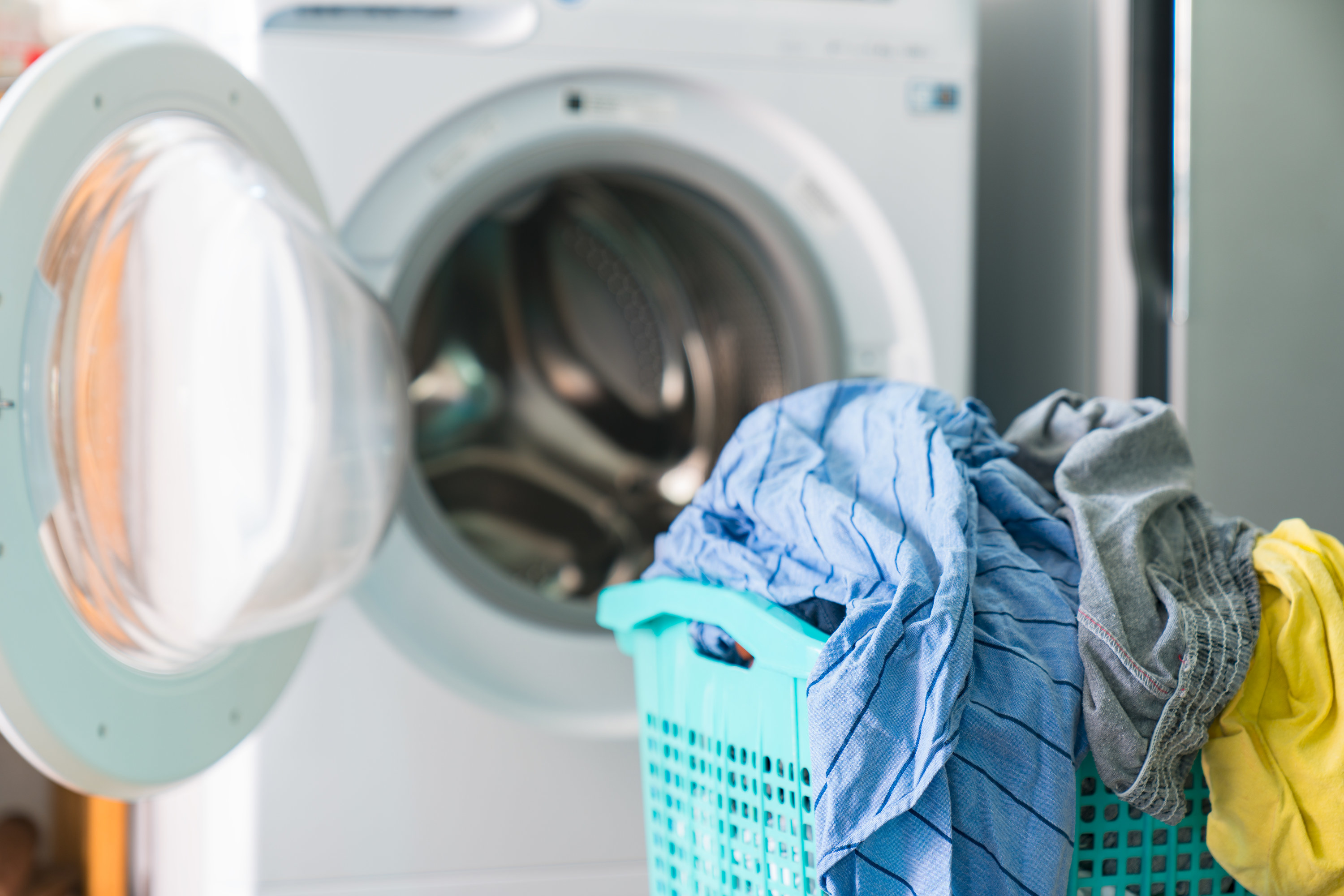 an open washing machine with a laundry basket in front of it