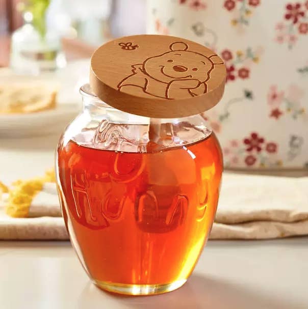 a glass jar that says "hunny" on it and is filled with honey with a winnie the pooh wooden lid
