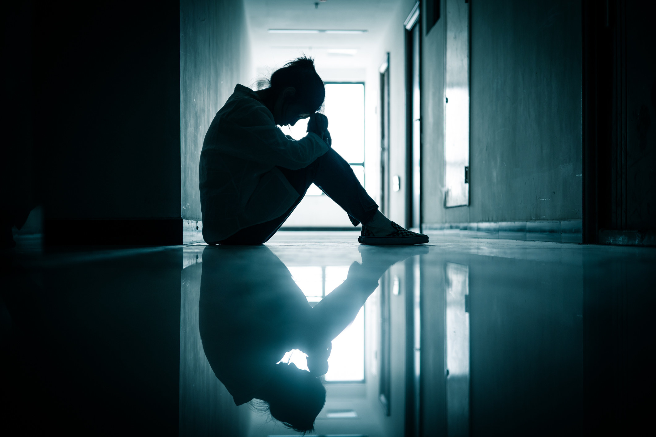 A woman sitting in a dark hallway with her head lowered