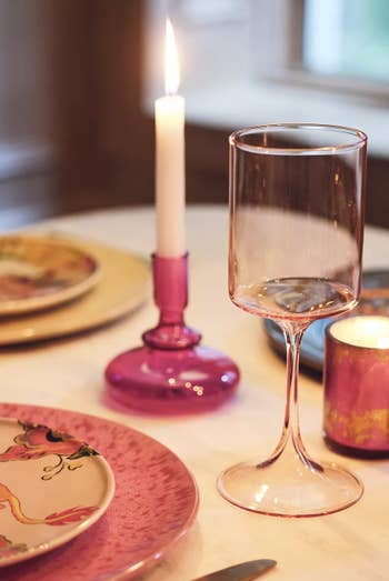 The pink wine glass at table setting with candle lit in background
