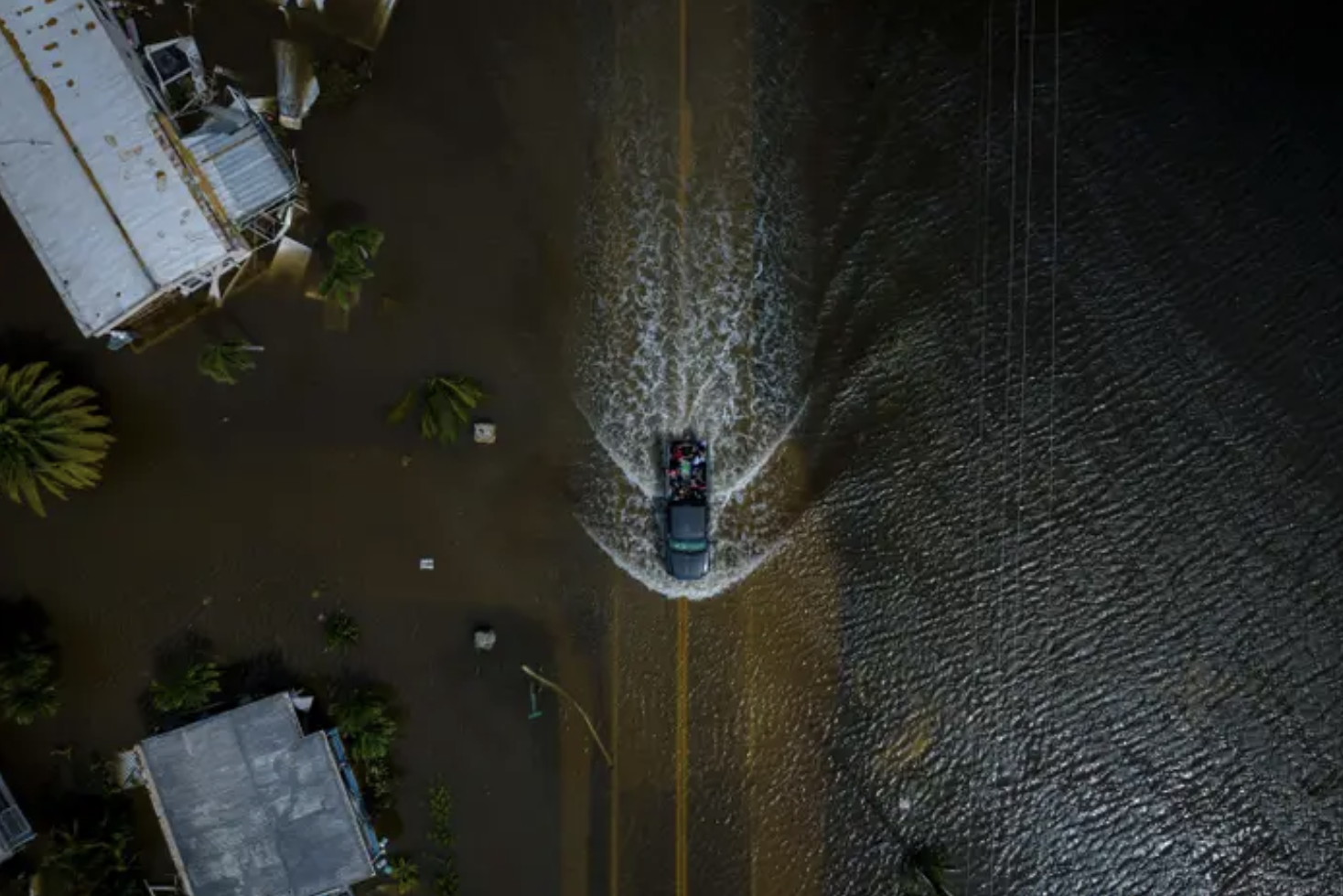 a car drives through completely flooded street