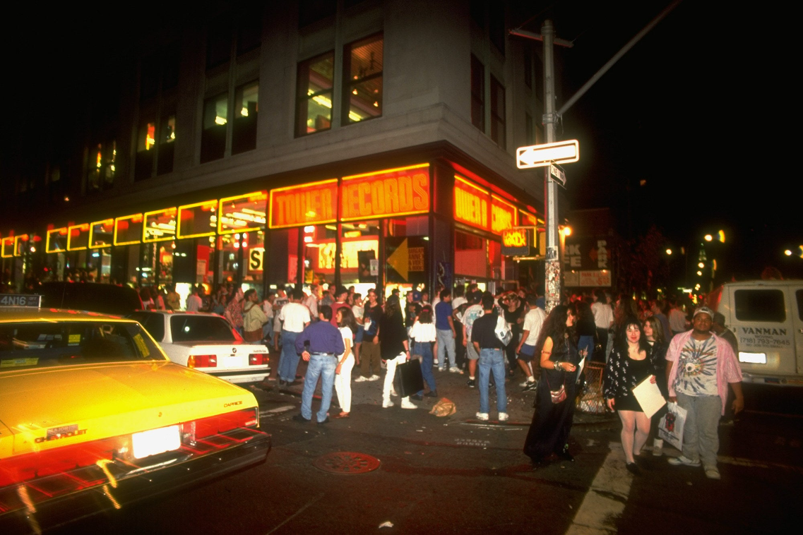 At night, a long line forms on a busy street outside a record store