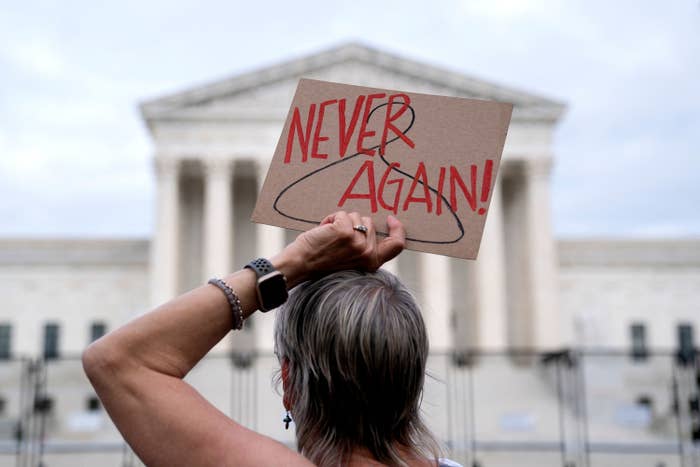 A person holding up a sign that has a drawing of a clothes hanger and the words "Never Again!"