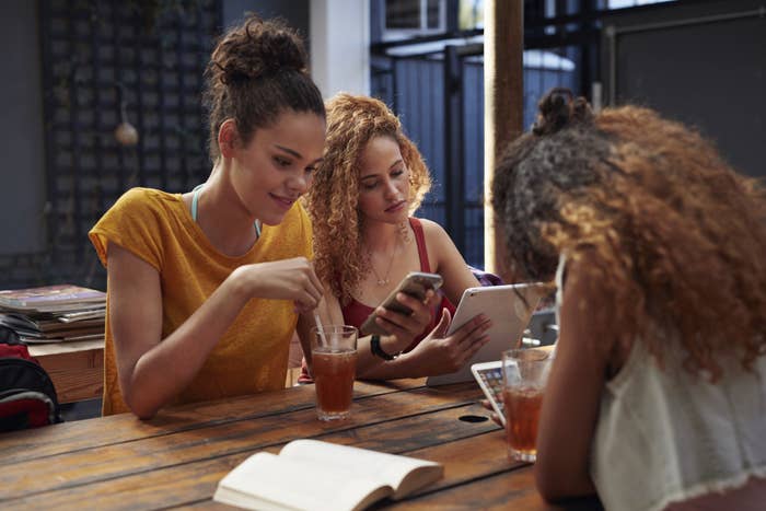 Young women sitting around a table and looking at their phones and tablets