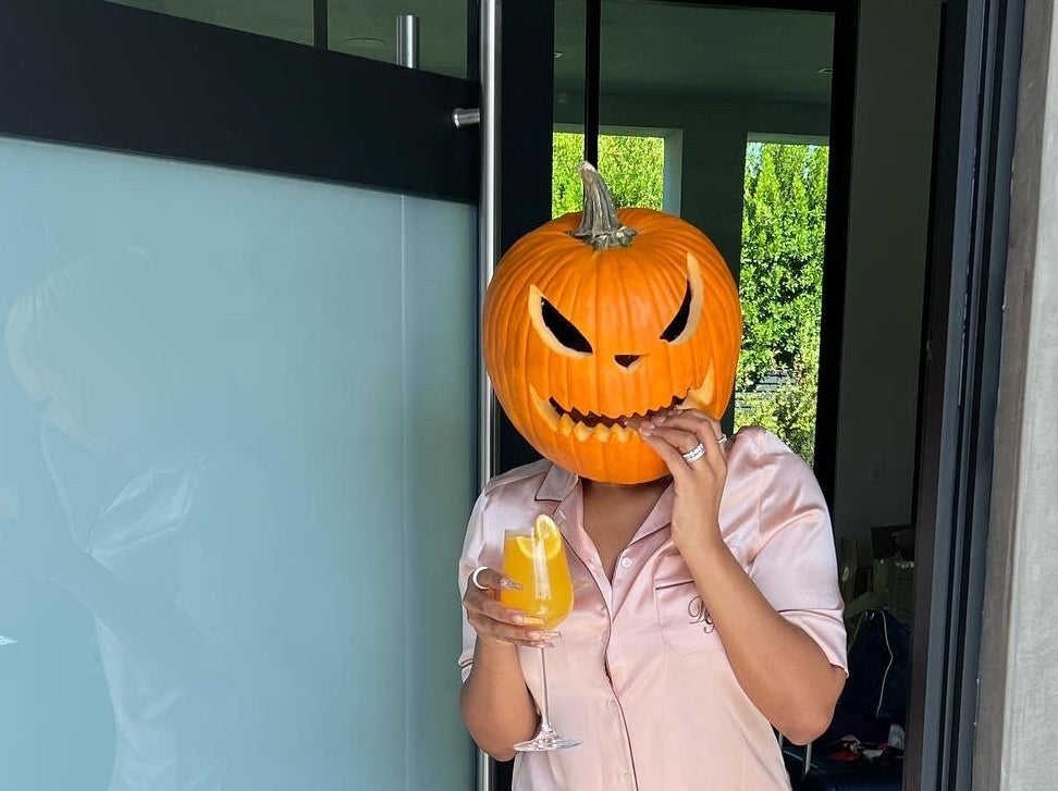 Megan wears the pumpkin on her head while standing by her front door