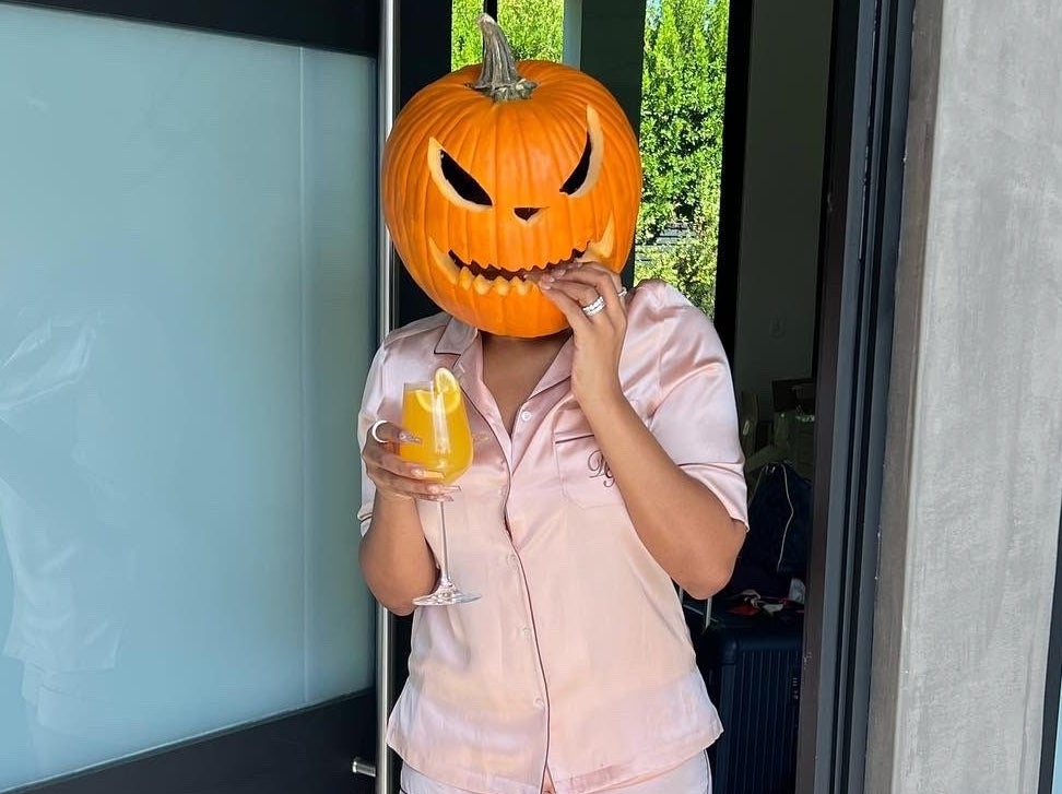 Megan wears the pumpkin on her head while standing by her front door