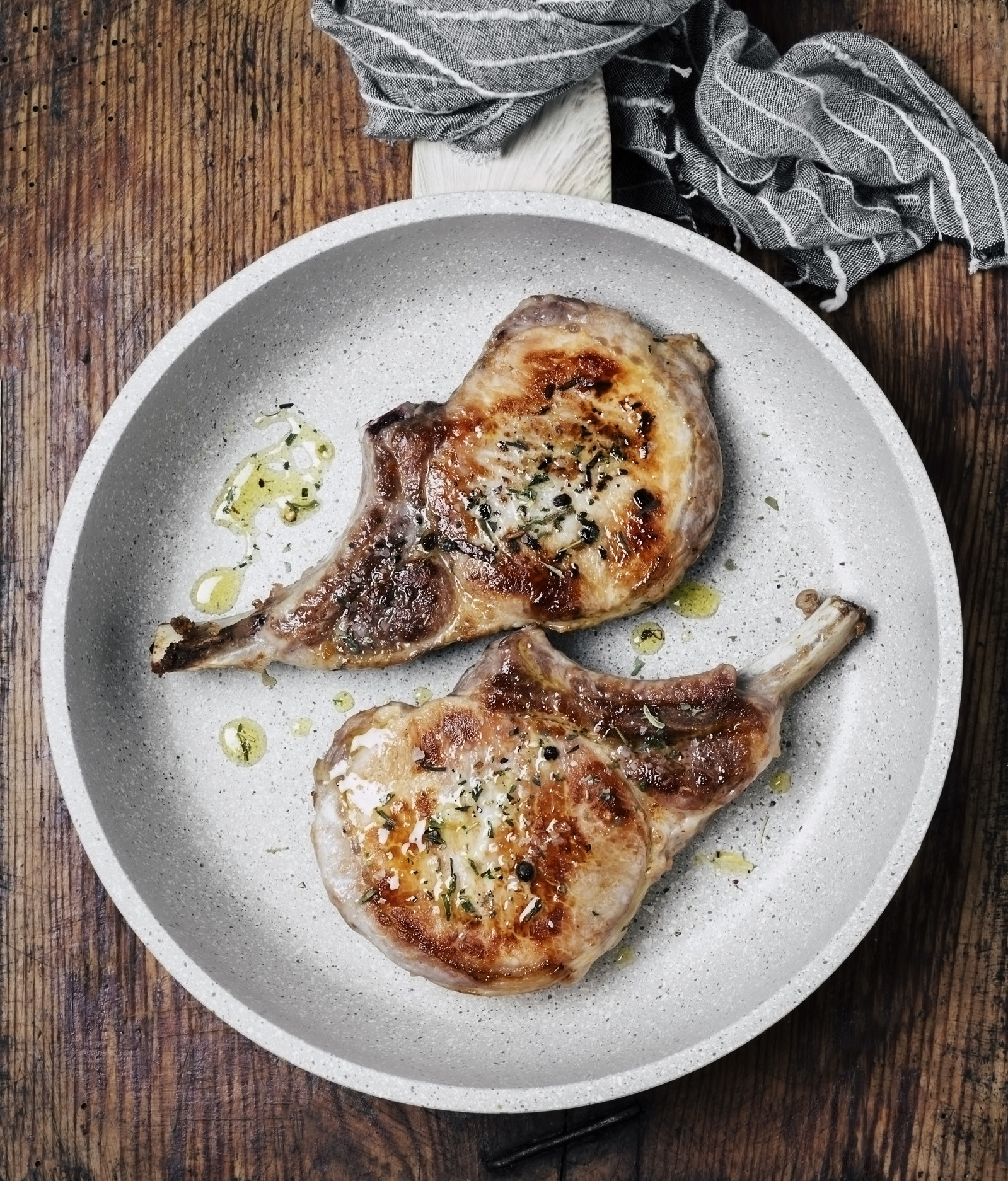Pork chops in a frying pan on wooden background.