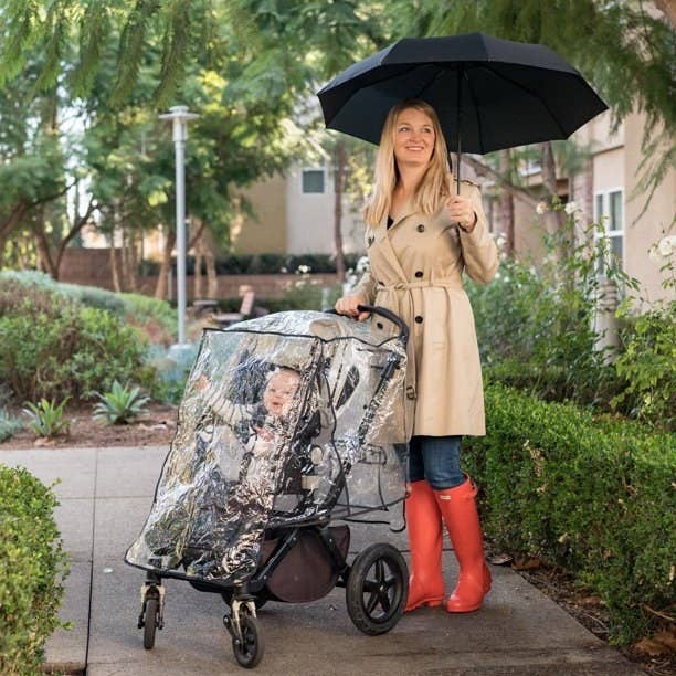 A person in rain gear pushes a baby in a stroller with the weather shield
