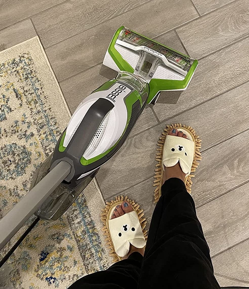 a reviewer wearing the bearing slippers while mopping 