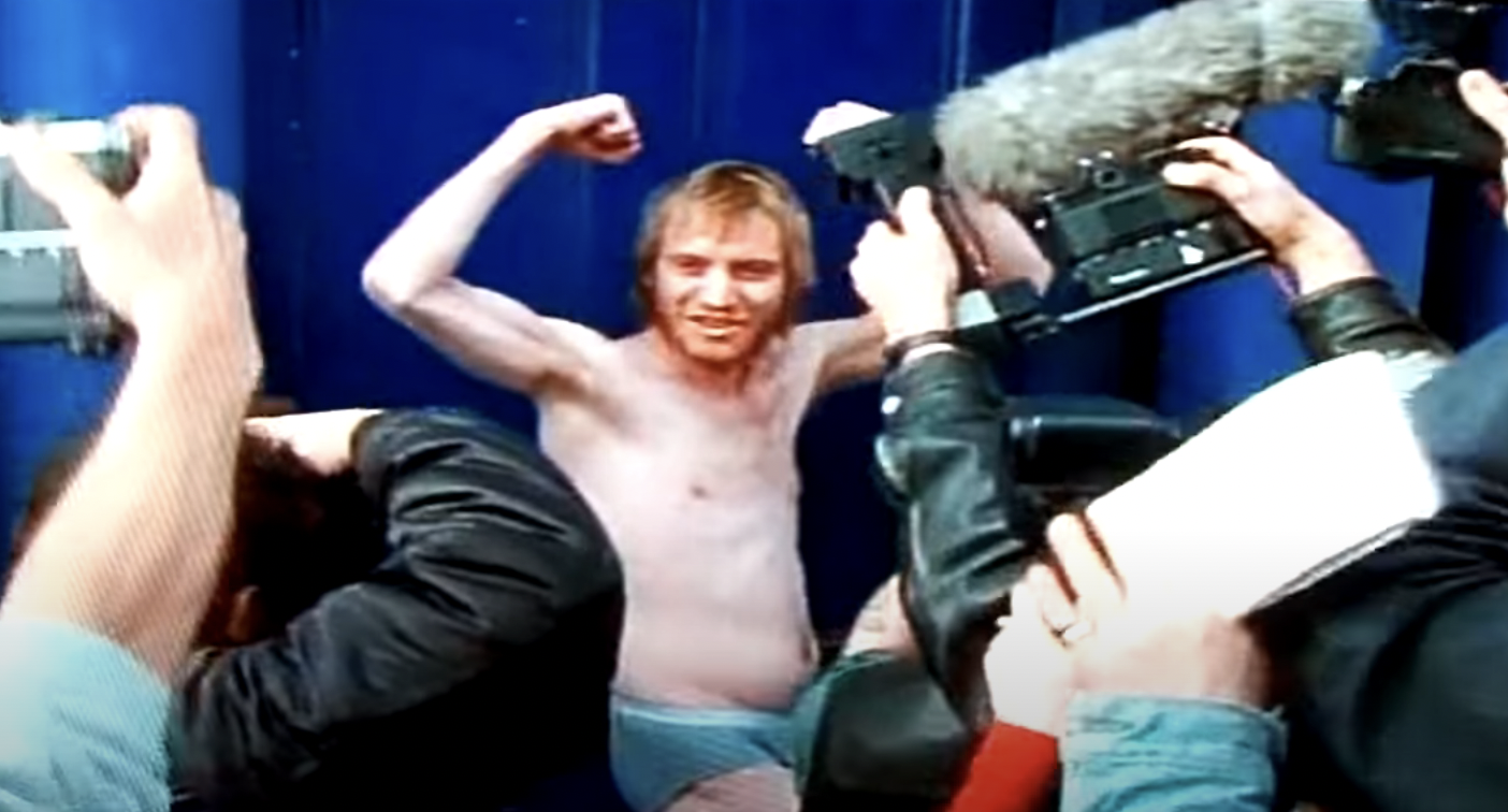 Rhys Ifans as Spike in Notting Hill standing on his doorstep and flexing his arms in his underwear with paparazzi cameras all around him