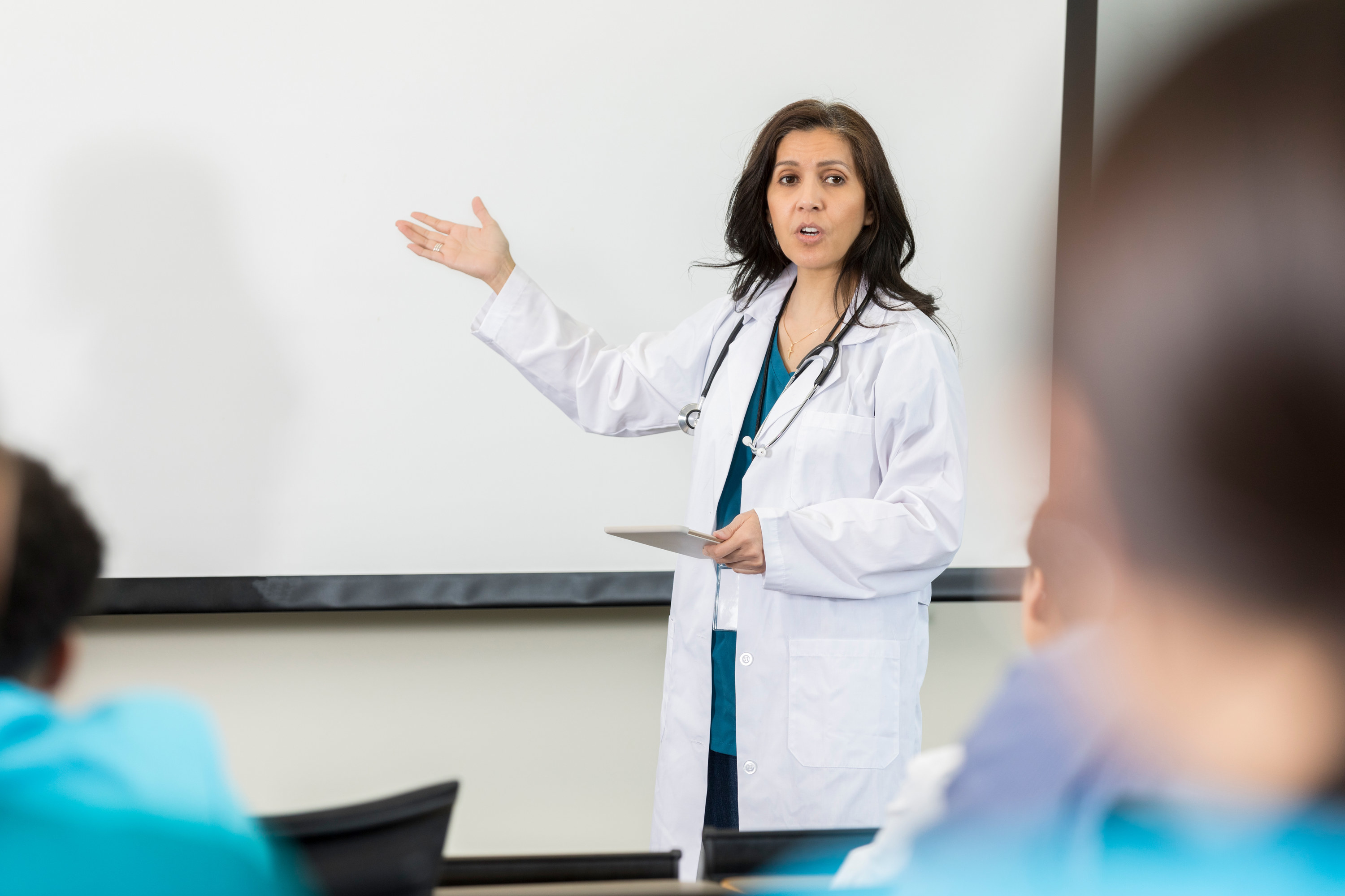 A medical professor points to a white board while giving a lecture