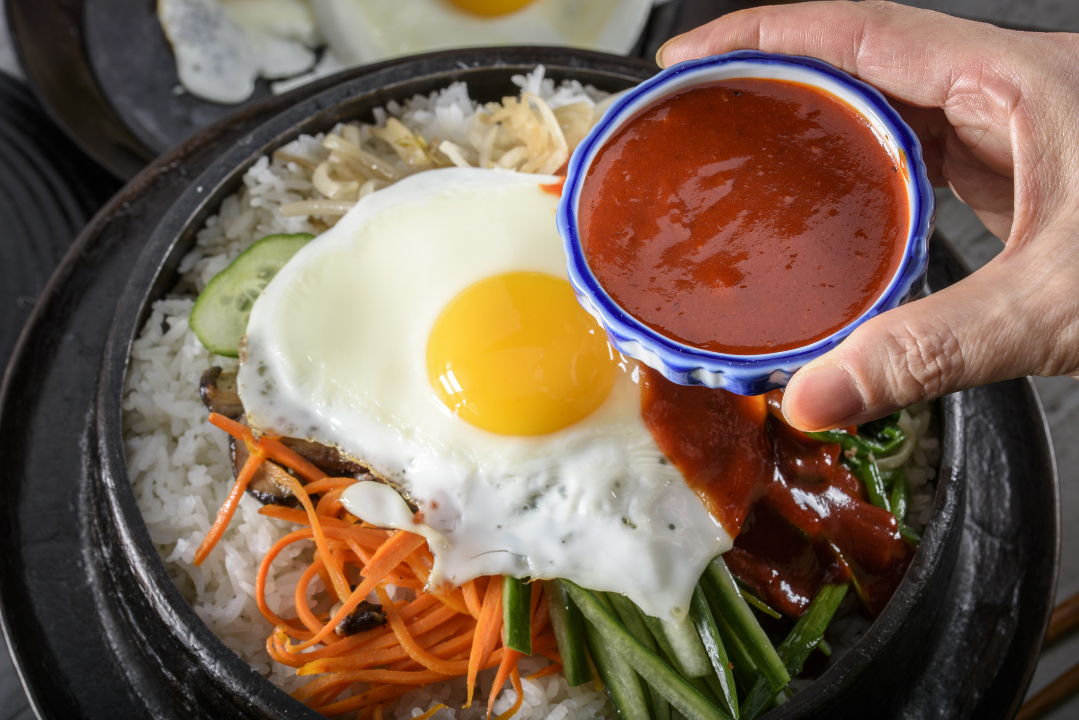 Korean bibimbap — including rice, carrots, other vegetables, a fried egg, and gochujang added to it
