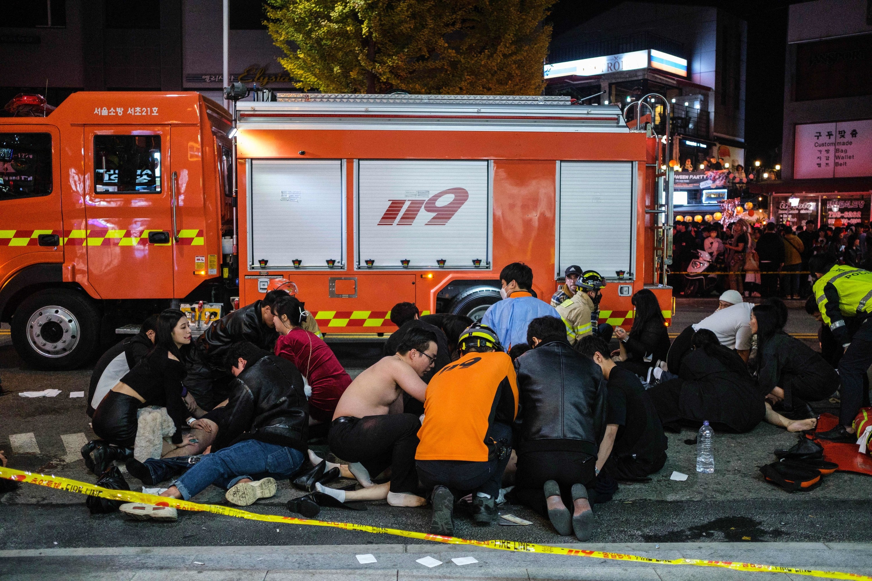 People lying on the ground as others kneel over them in front of a large vehicle