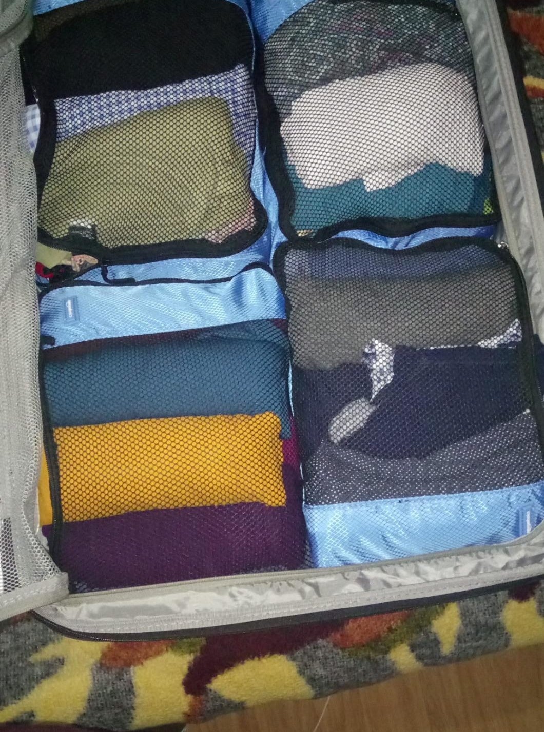 reviewer&#x27;s suitcase filled with four of the packing cubes, each containing neatly rolled clothes