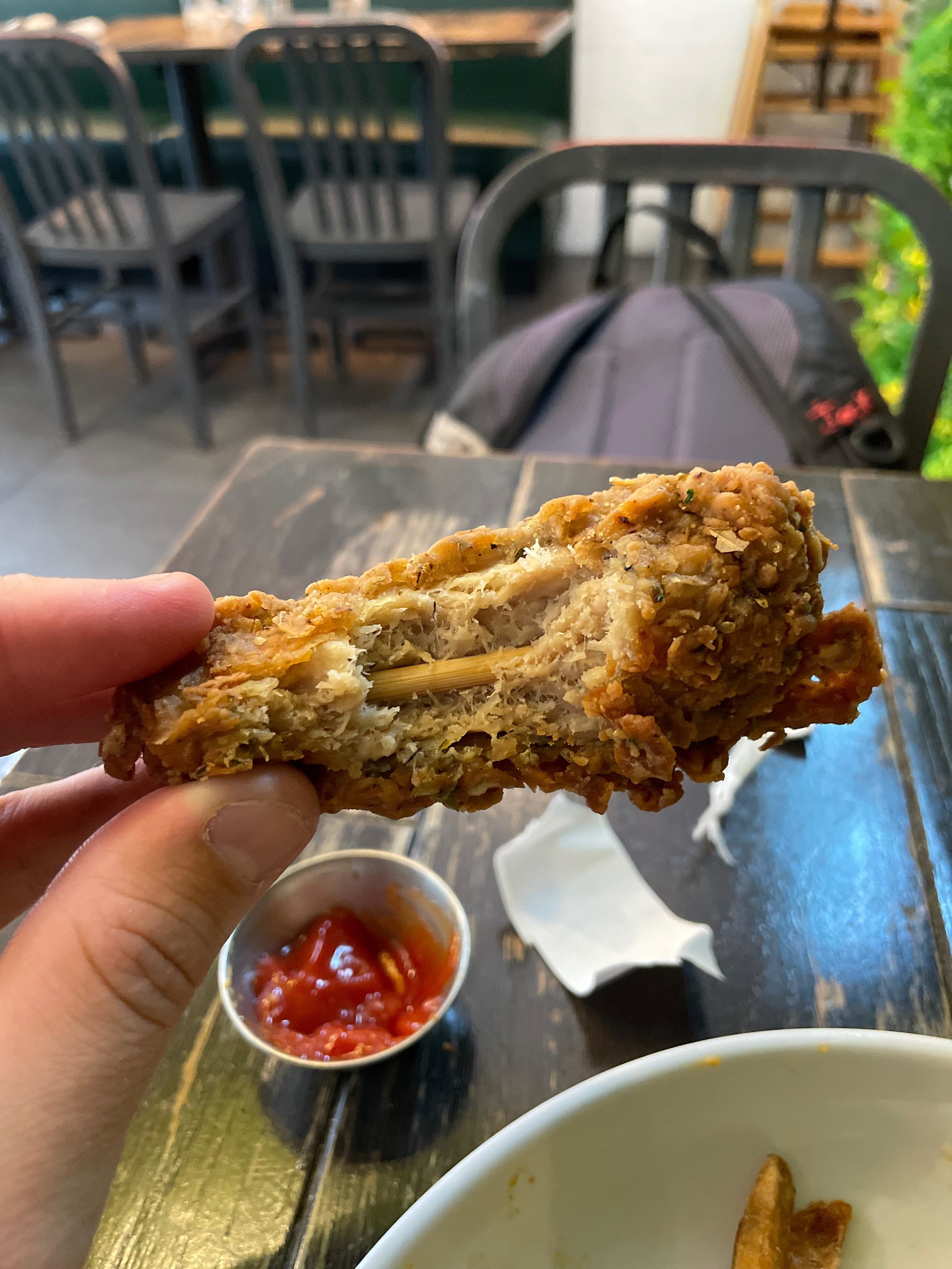 Someone holding a vegan chicken wing with the interior visible, showing a wooden bone