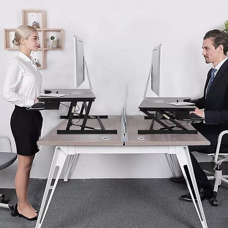 A model using the desk and standing and another model using the desk sitting down