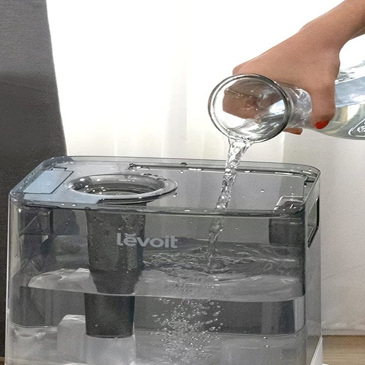 a person pouring water into the top of the humidifier tank