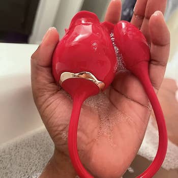 Reviewer holding red rose-shaped dual-ended vibrator in bathtub