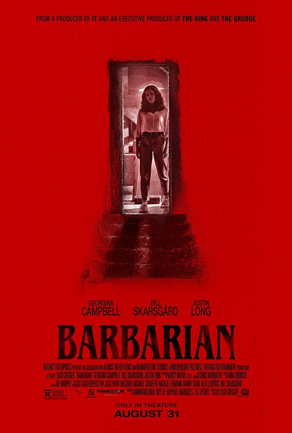 The movie poster for Barbarian. The poster is primarily red, with Georgina Campbell&#x27;s character Tess standing in a doorway to a basement with stairs leading down that fade out.