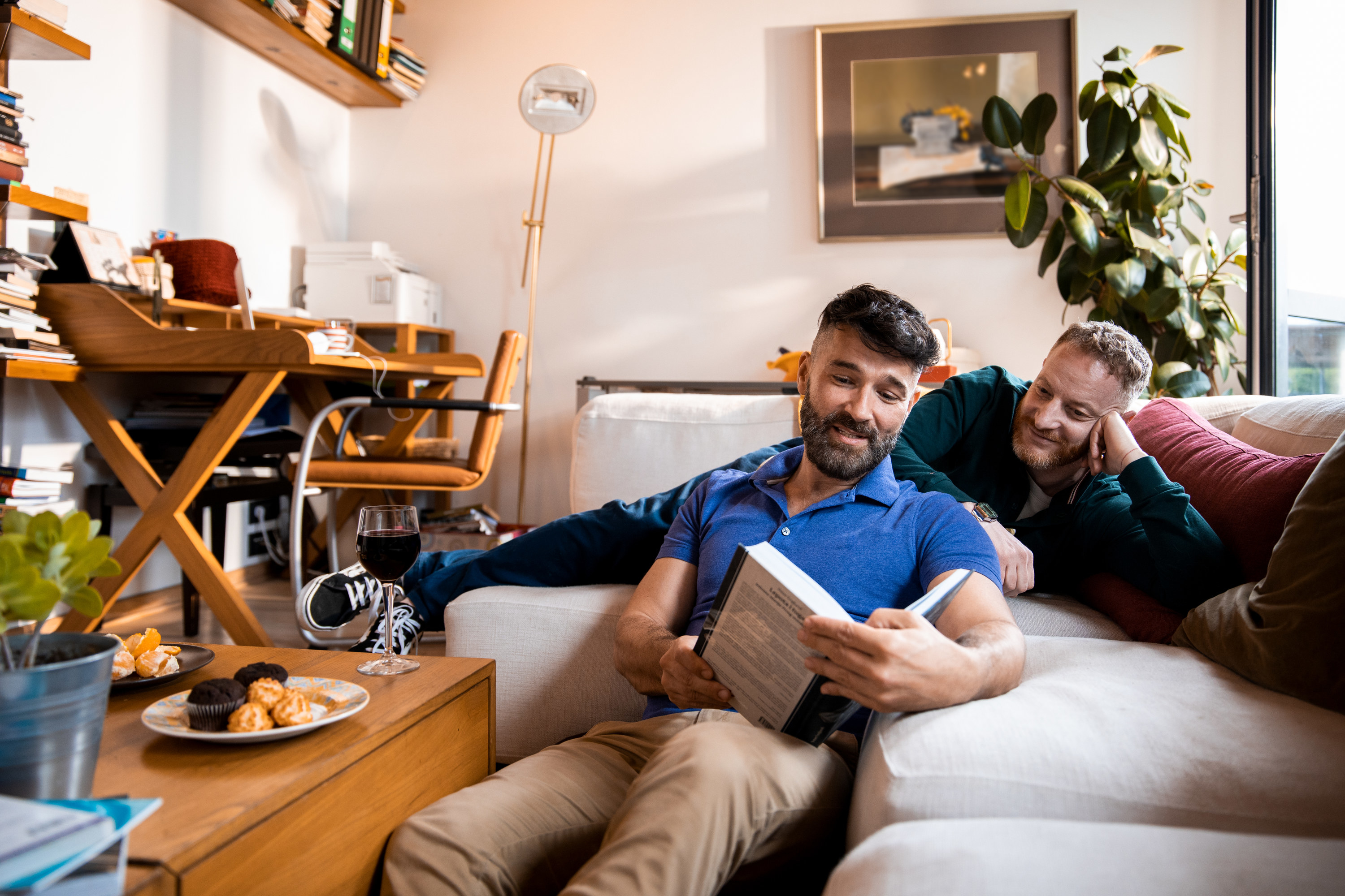 Two men on a couch reading a book.