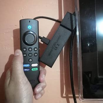 a reviewer holding the included remote up to the plugged in Fire Stick