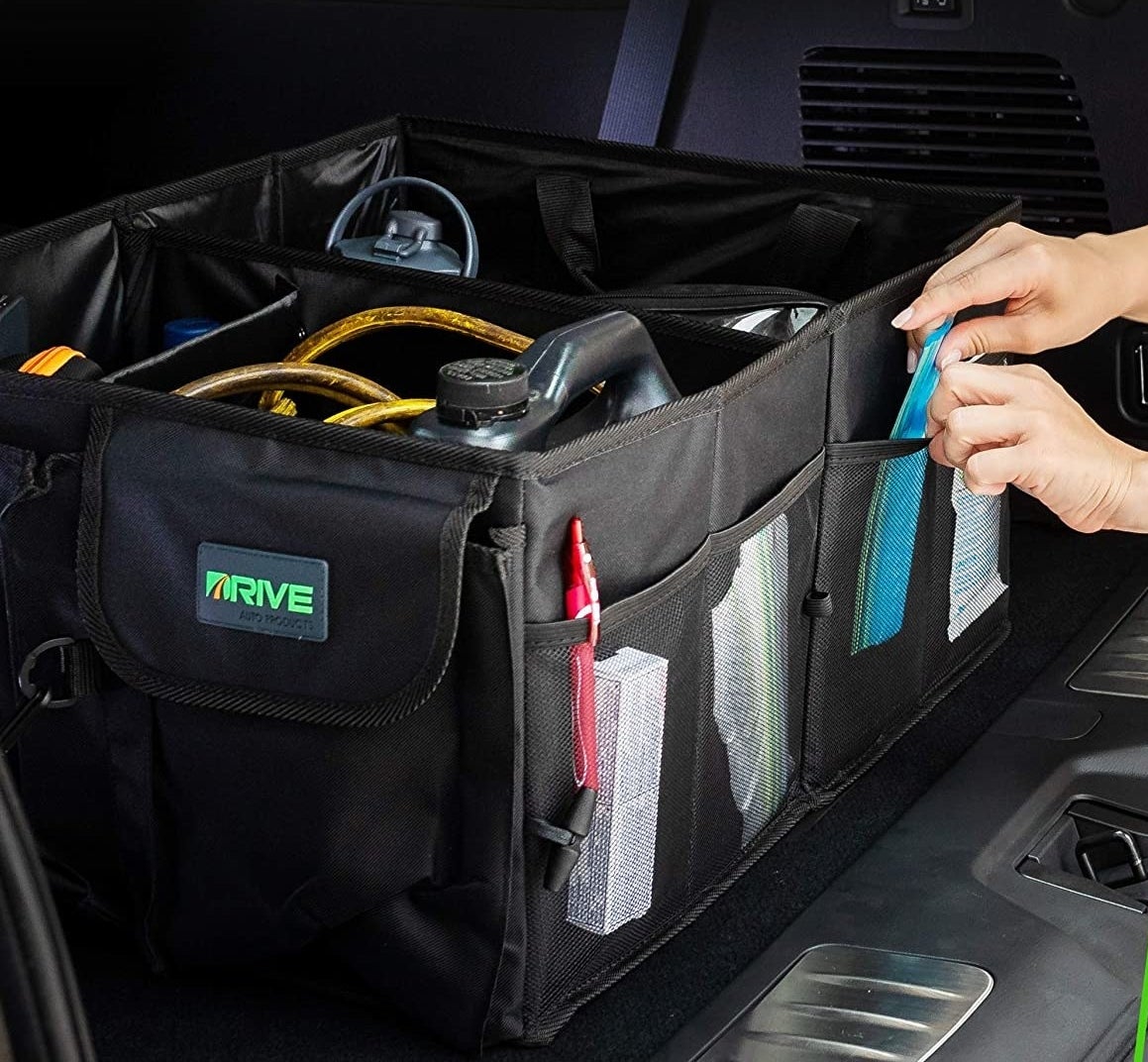 the organizer in a trunk filled with things and someone putting something in one of the pockets