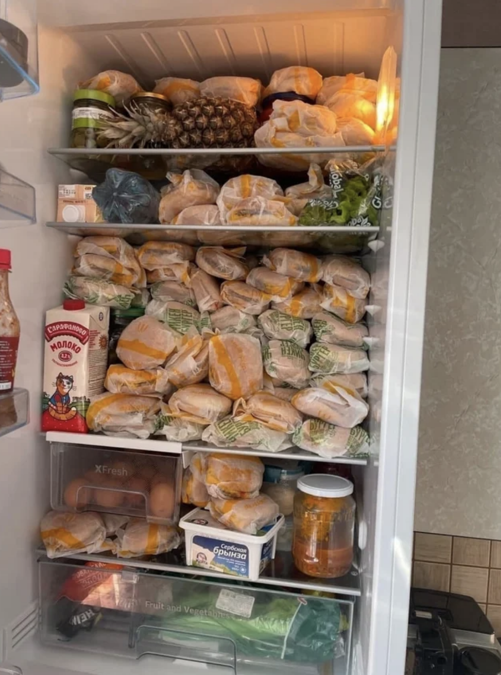 A refrigerator packed with wrapped burgers alongside other food