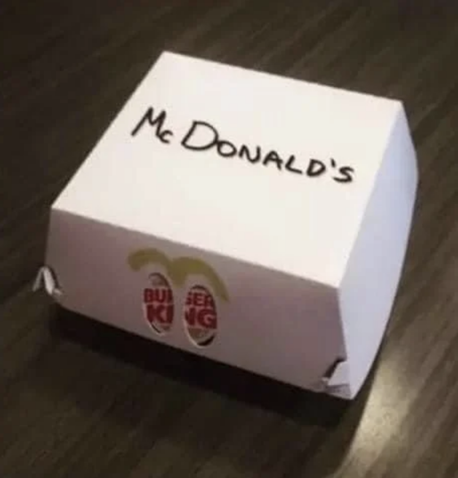 A takeout box with &quot;McDonald&#x27;s&quot; written on it, with the Burger King logo visible through two &quot;eye&quot; holes